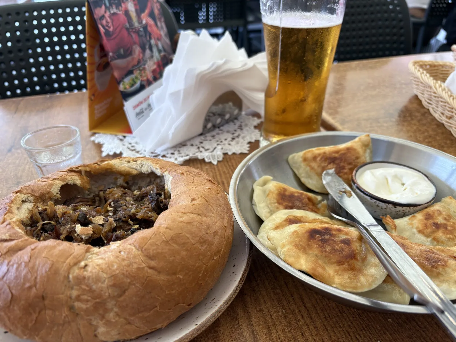 ポーランド料理。パンに入ったビゴスと、ヨーグルトソースを添えた焼きピエロギ、ビール