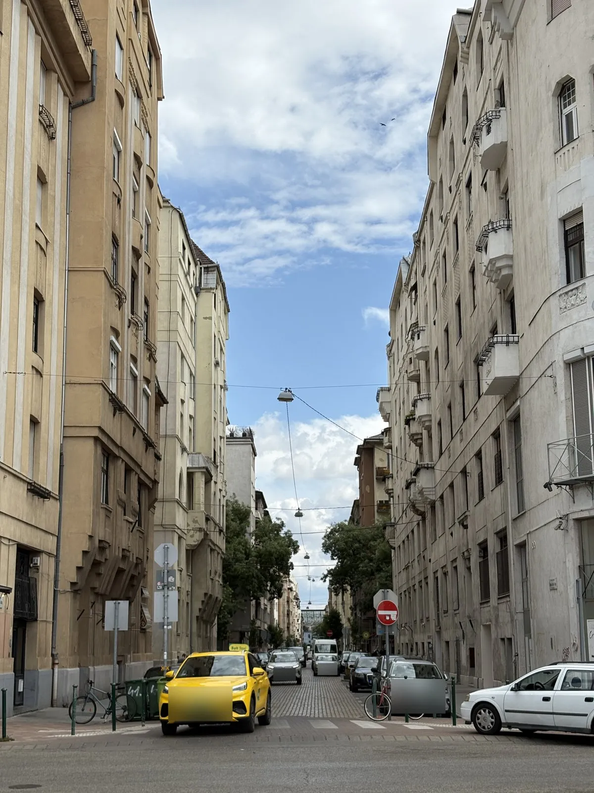 ブダペストの通り。古い集合住宅が両側に続き、黄色い車が停まっている
